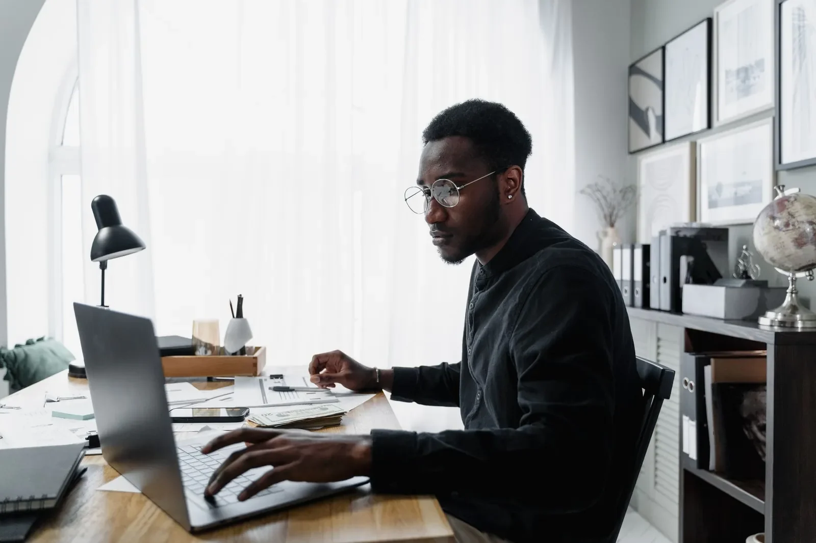A man in glasses working at a laptop in a bright office.