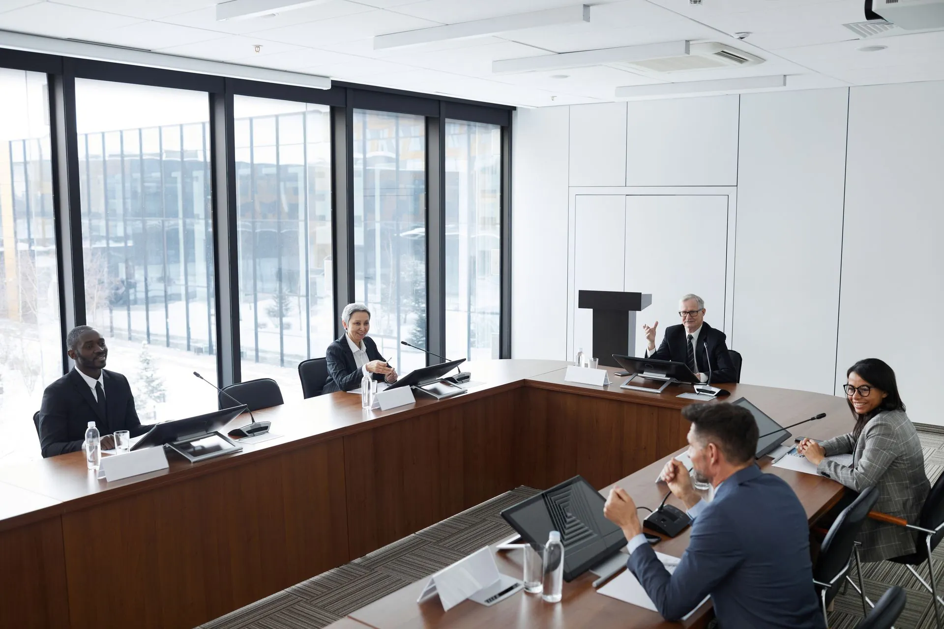 Officials seated around a long meeting table in a bright room with a podium and tall windows.